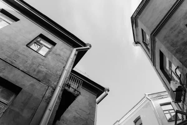Upward view of weathered residential buildings with windows and metal downspout