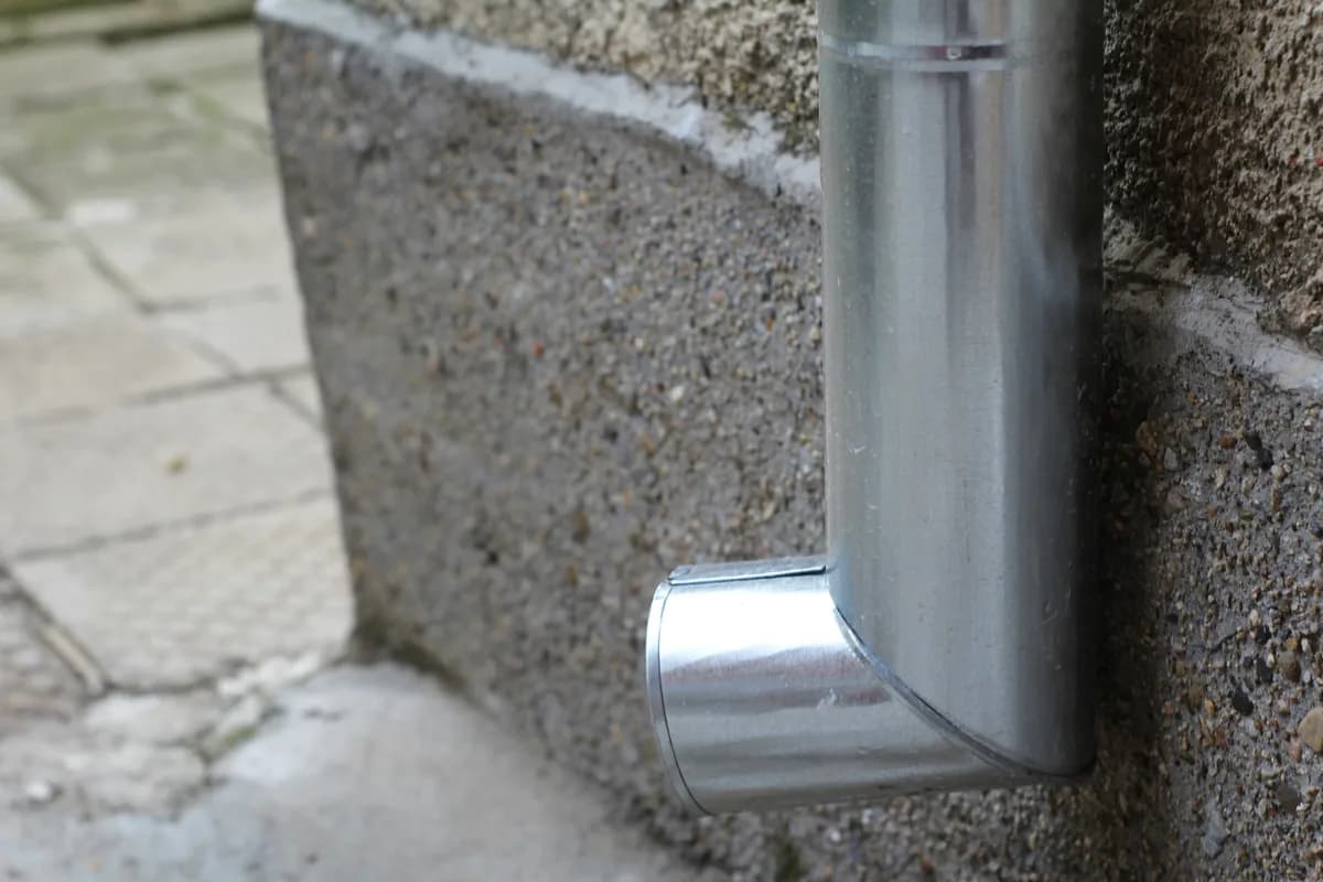 Metal downspout elbow attached to concrete foundation wall outdoors