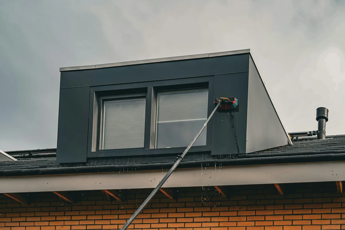 Worker cleaning windows on modern rooftop structure with extension pole