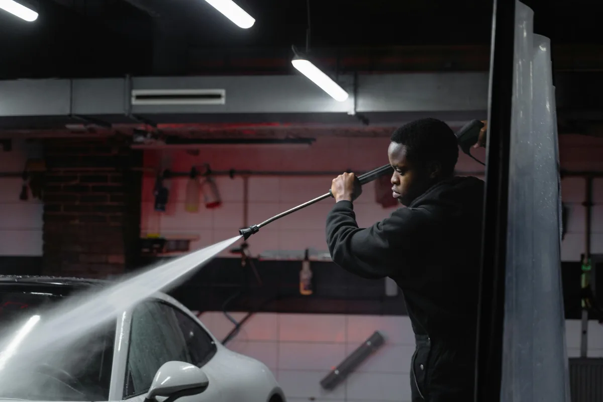 Worker cleaning car window with squeegee tool at night facility