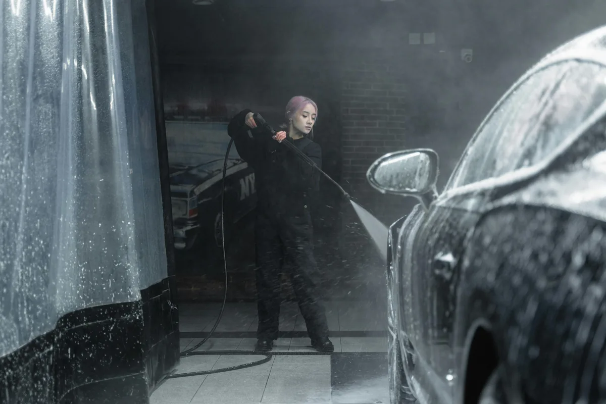 worker using pressure washer spray cleaning wet vehicle exterior surface