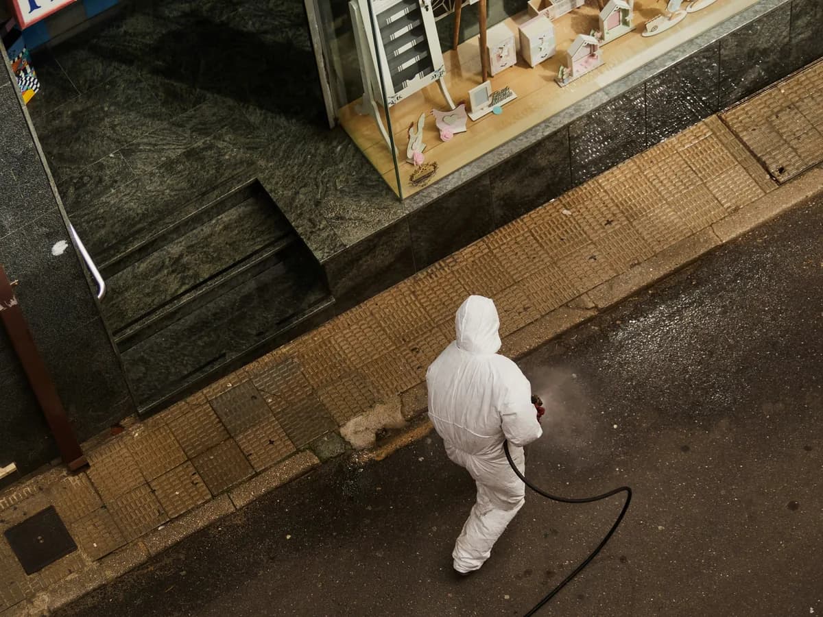 worker in protective suit spraying storefront pavement with cleaning hose