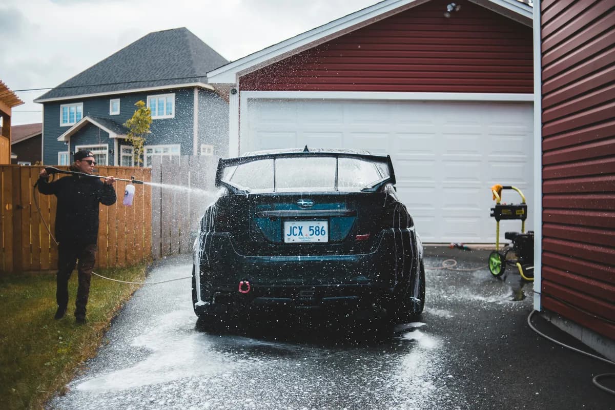Man washing dark car with pressure washer near residential garage