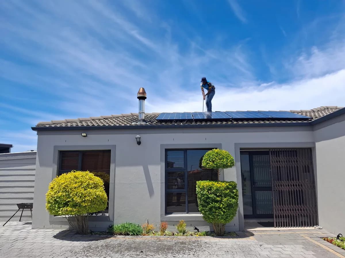 Worker installing solar panels on residential house roof under blue sky