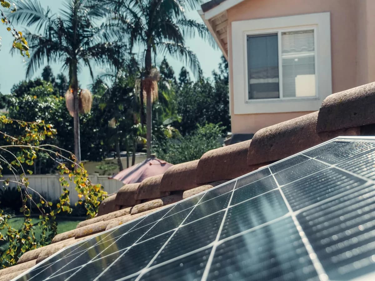 Solar panels installed on residential roof with house and palm trees visible