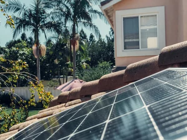 Solar panels installed on residential roof with house and palm trees visible