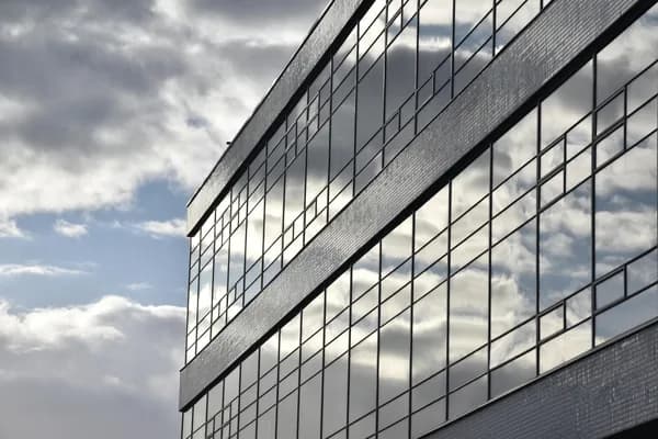Modern office building facade with reflective glass windows and cloud reflections