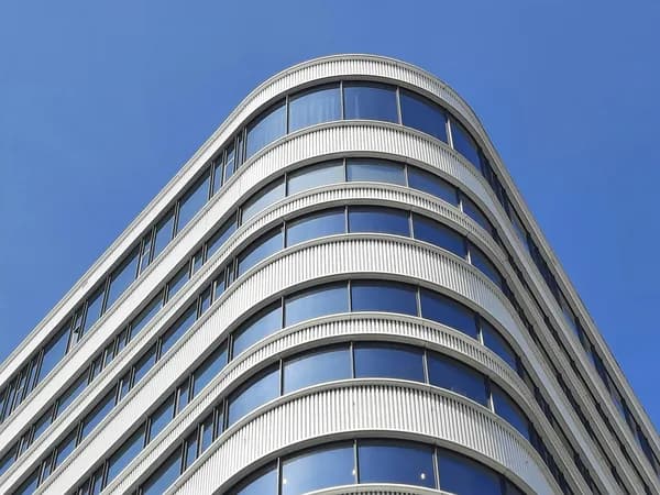 Modern curved commercial building facade with clean reflective windows against blue sky