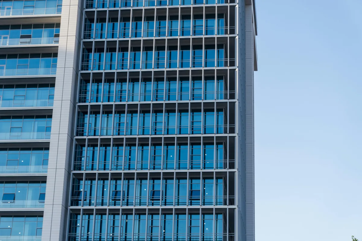 Modern glass and steel office building facade with reflective windows and clear sky