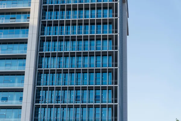 Modern glass and steel office building facade with reflective windows and clear sky