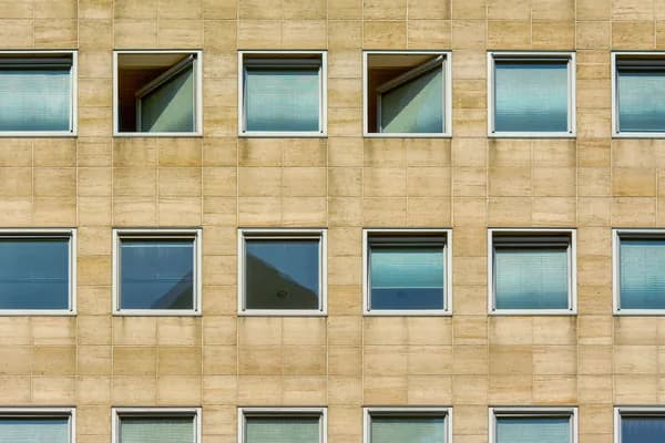 Modern sandstone building facade with rows of clean windows and blinds