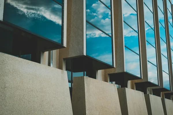 Modern glass windows reflecting sky on concrete brutalist building facade