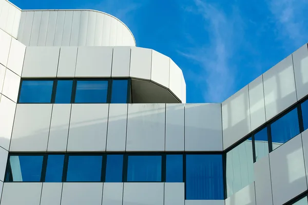 Modern building exterior with large windows and white metal panels under blue sky