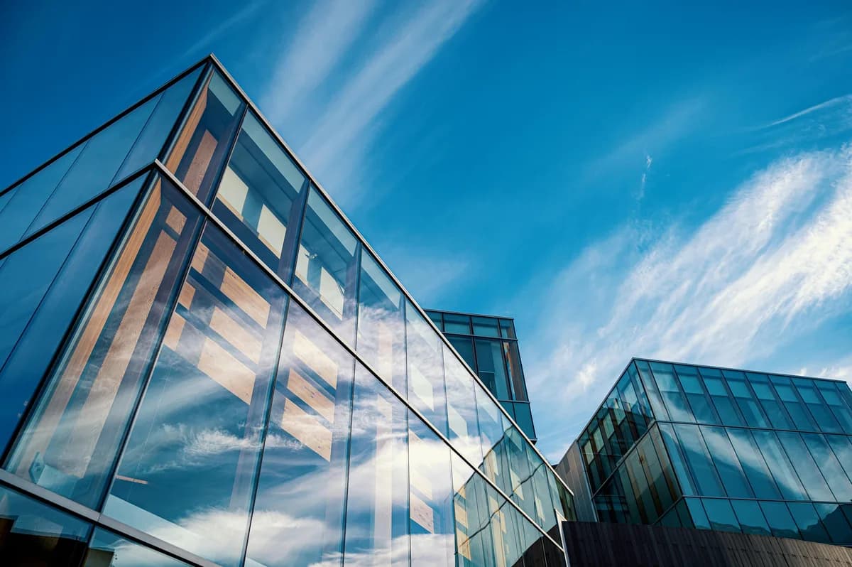 Modern glass building facade reflecting blue sky and clouds above