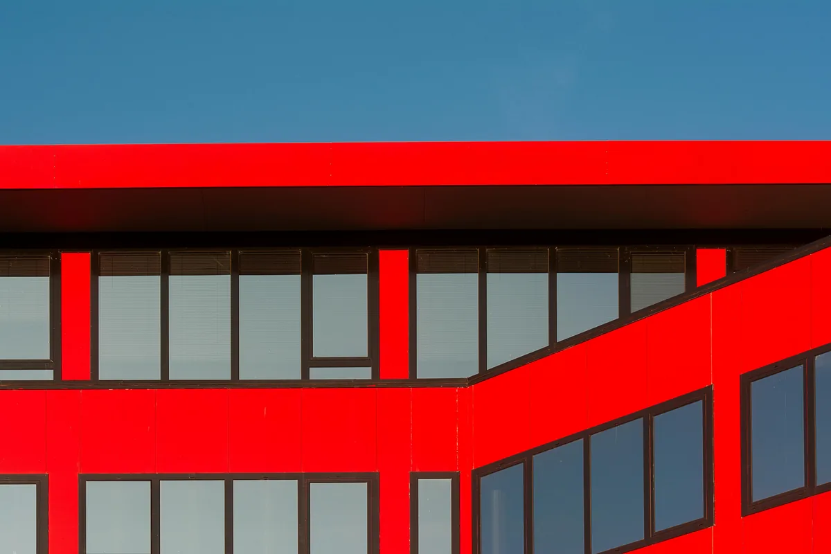 Modern red building facade with multiple rows of large glass windows