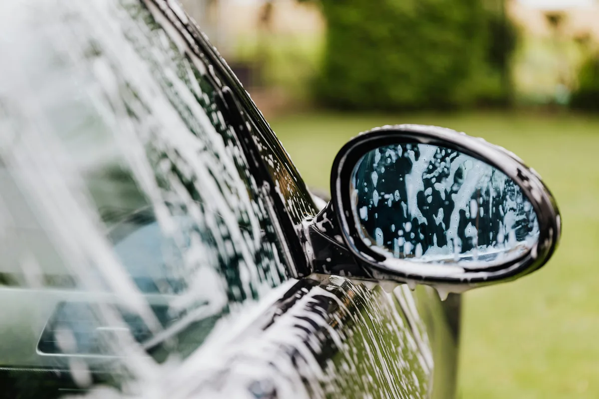 Car side mirror covered in water droplets during vehicle washing outdoors