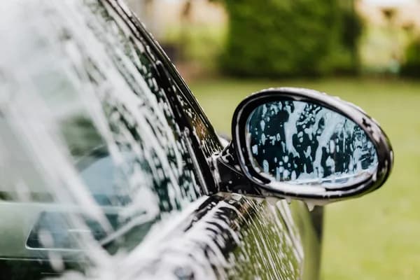 Car side mirror covered in water droplets during vehicle washing outdoors