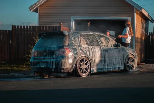 People washing car with water spray in residential driveway setting