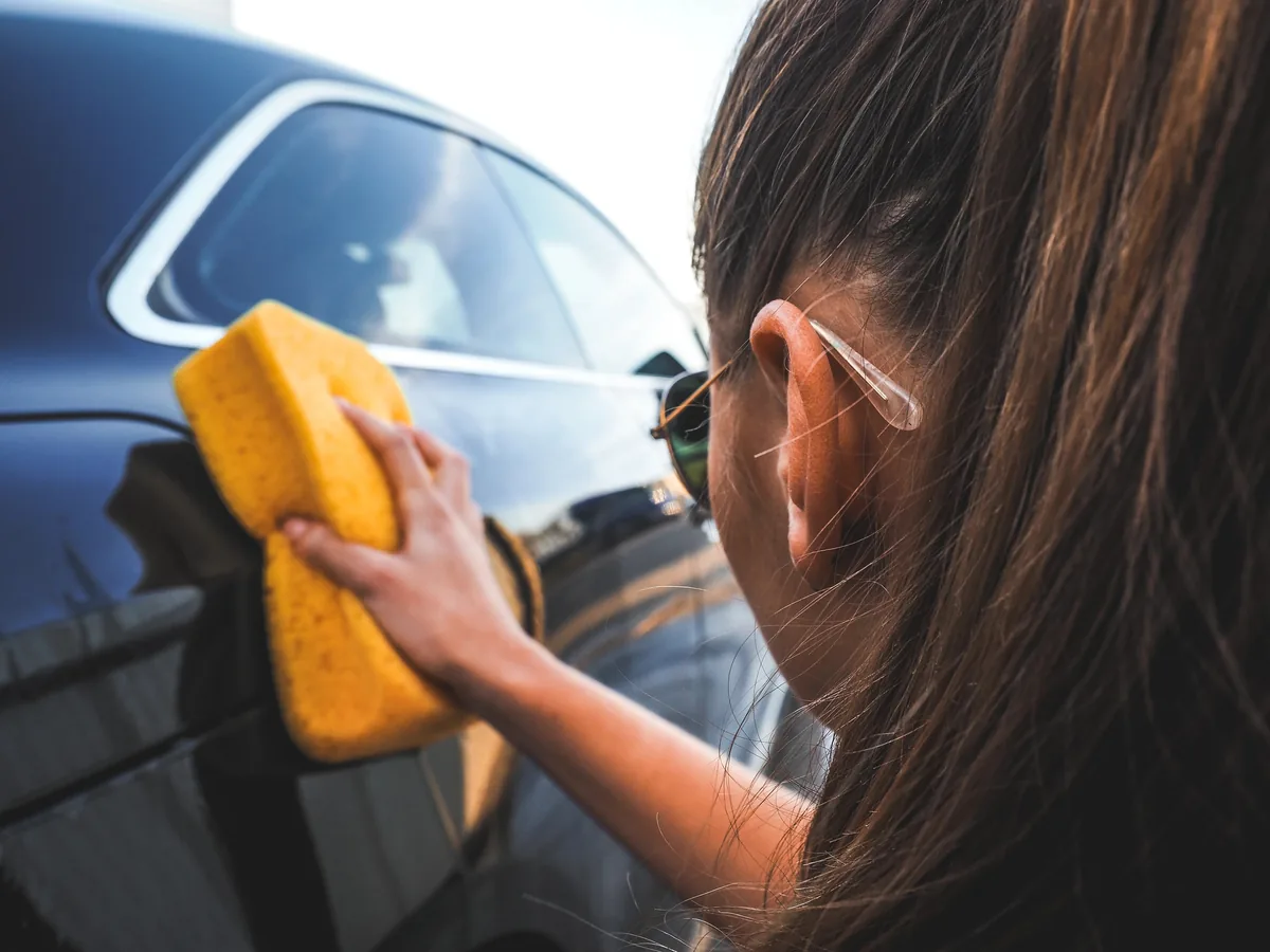 Woman cleaning car window with yellow microfiber cloth outdoors