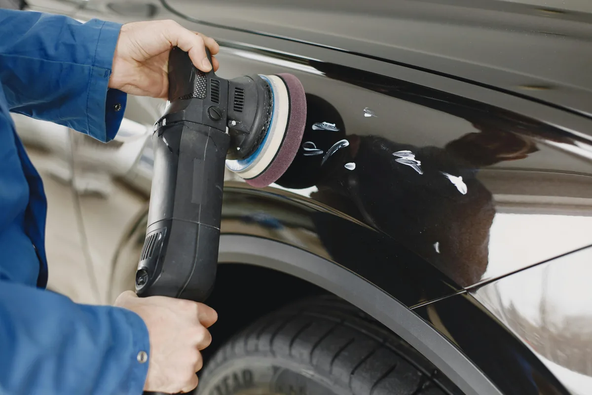 Worker using orbital buffer machine to polish car exterior surface