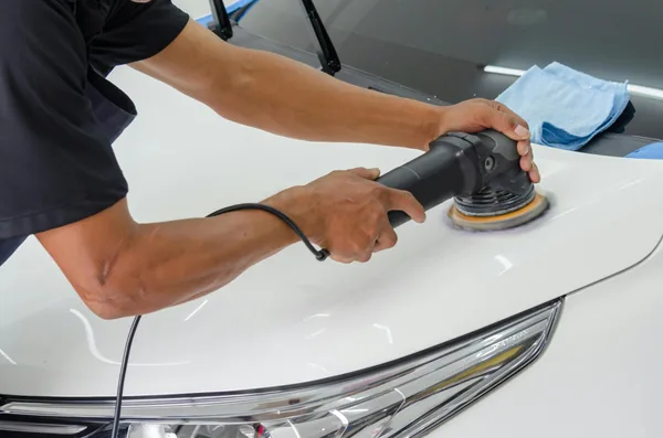 Professional using orbital polisher on white car hood with microfiber cloth