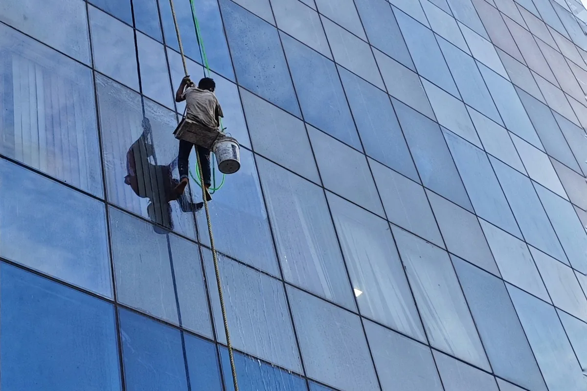 window cleaner suspended by rope cleaning exterior glass facade of modern building