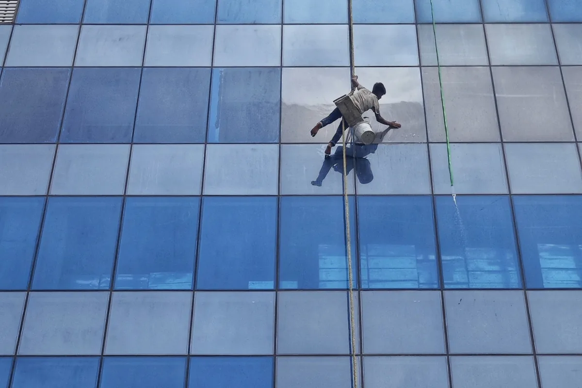 window cleaner suspended by rope cleaning large glass building facade
