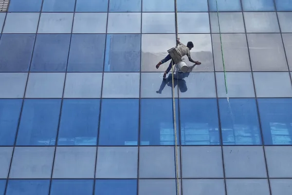 window cleaner suspended by rope cleaning large glass building facade
