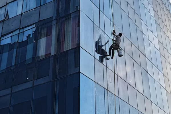 Window cleaner suspended by rope cleaning exterior glass of tall modern building