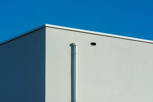Modern white building exterior with metal pipe against clear blue sky