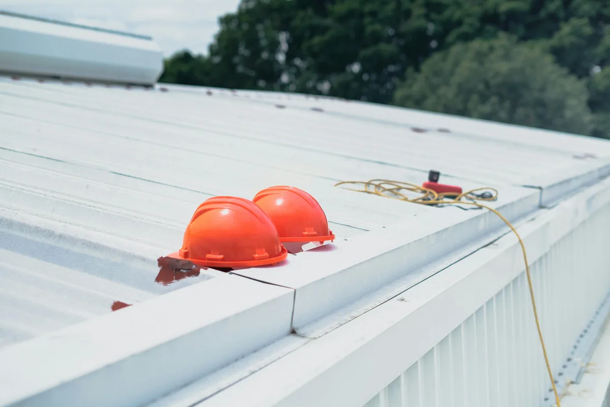Two orange hard hats and rope on white commercial roof surface