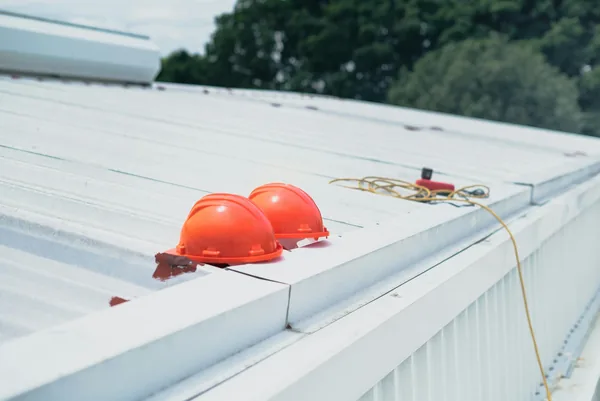 Two orange hard hats and rope on white commercial roof surface