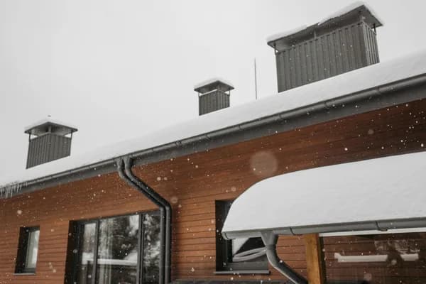 Snow-covered wooden residential roof with metal chimneys and gutters