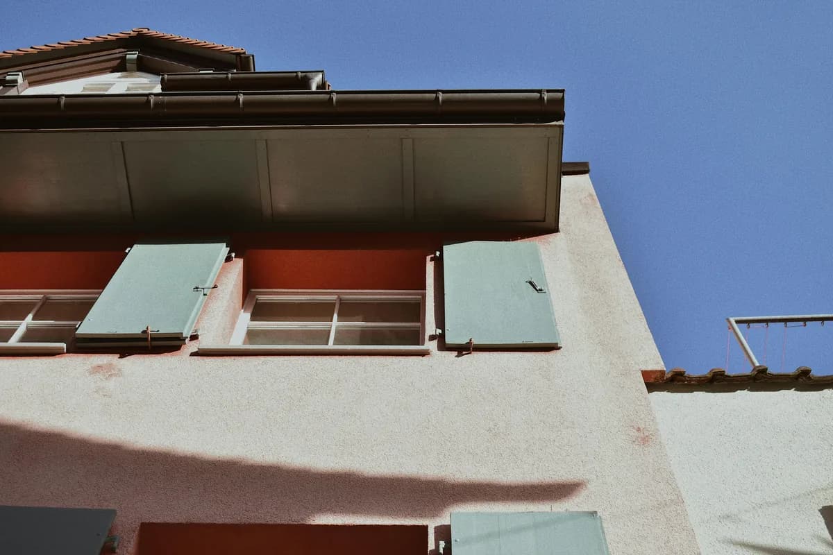 Multi-story residential building exterior with windows and metal gutters against blue sky