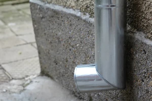 Metal downspout elbow attached to concrete foundation wall outdoors