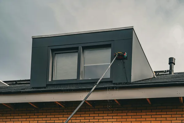 Worker cleaning windows on modern rooftop structure with extension pole