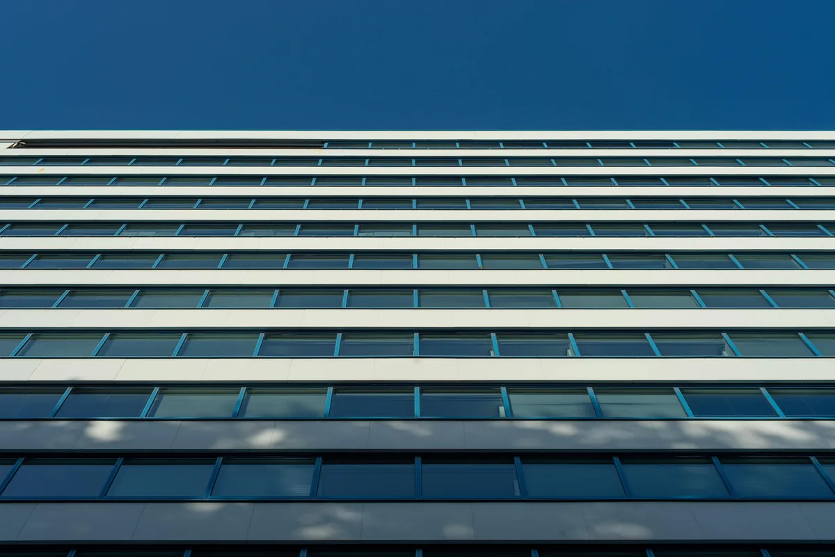 Modern commercial building facade with rows of blue tinted glass windows and white horizontal bands