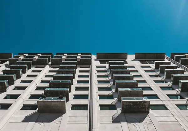 Modern high-rise building facade with rows of windows and balconies against blue sky