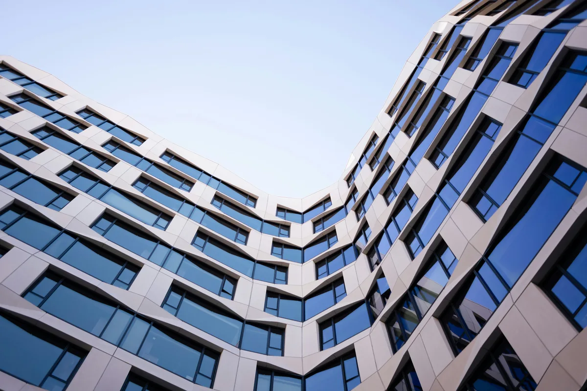 Modern curved building exterior with rows of large clean windows reflecting blue sky