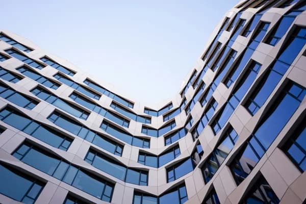 Modern curved building exterior with rows of large clean windows reflecting blue sky