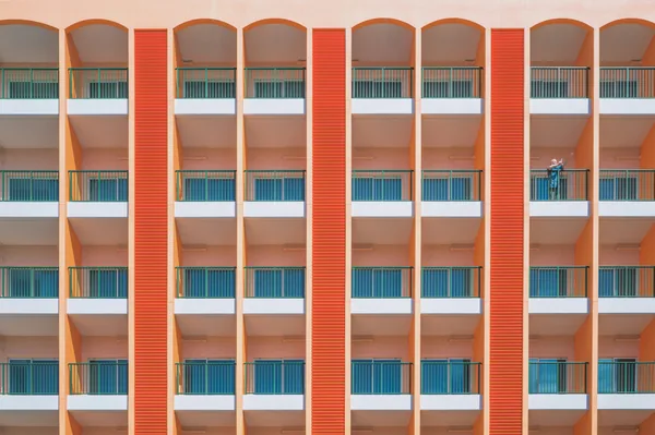 Worker on balcony of modern residential building with orange facade and blue railings