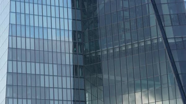 Modern glass building facade with gridded windows reflecting sky and clouds