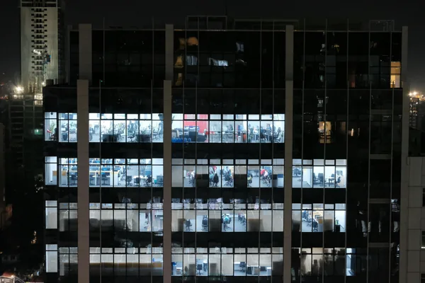 Nighttime office building facade with illuminated windows showing interior workspaces