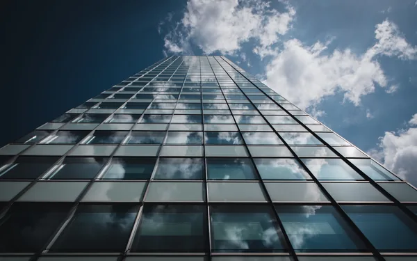 Modern skyscraper glass facade with reflective windows and cloudy sky