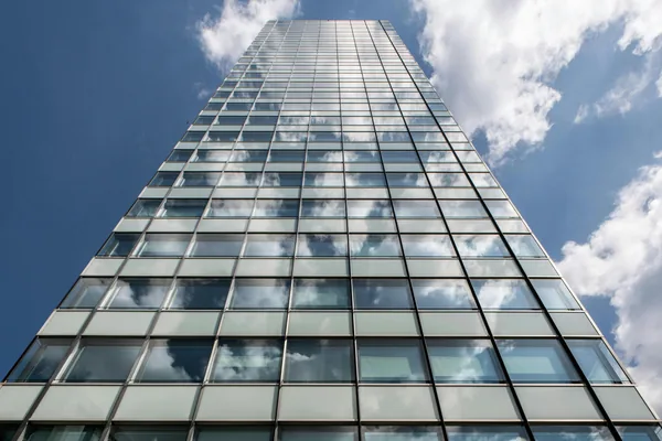 Tall modern glass building facade with reflective windows and sky
