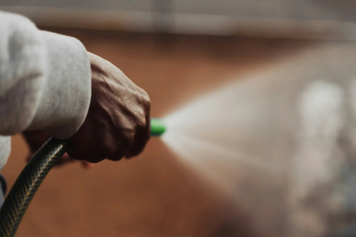 Gloved hand holding hose spraying water for cleaning purposes