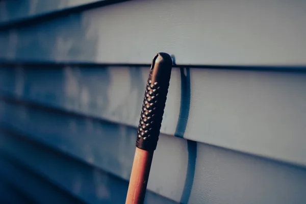 Close-up of window cleaning tool with black grip against white siding
