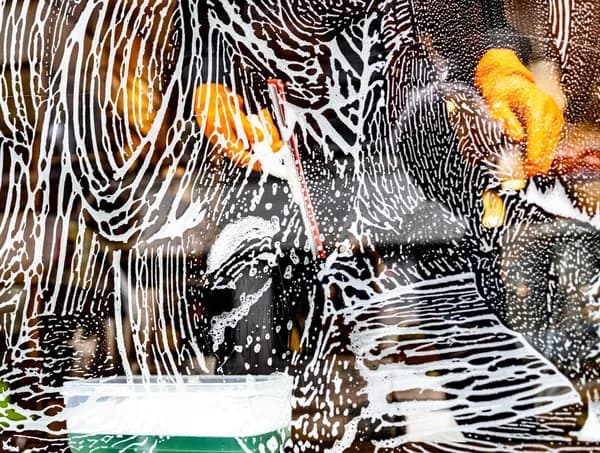 window cleaner using squeegee and soapy water on large glass surface