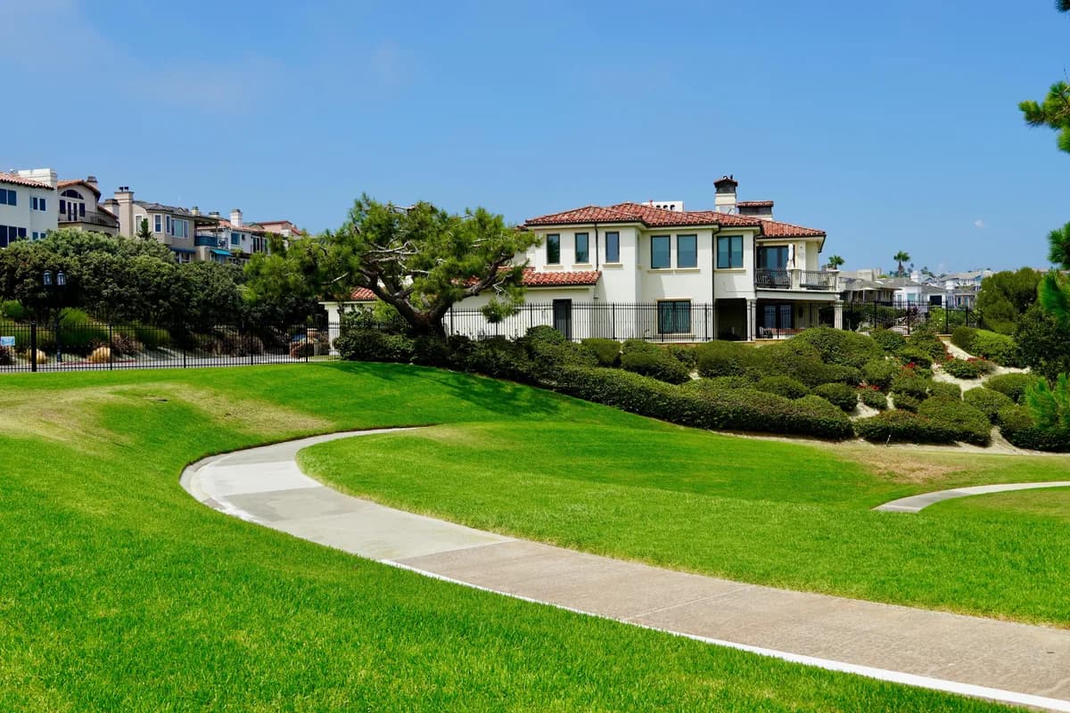 Large white Mediterranean-style home with manicured lawn and curved concrete pathway