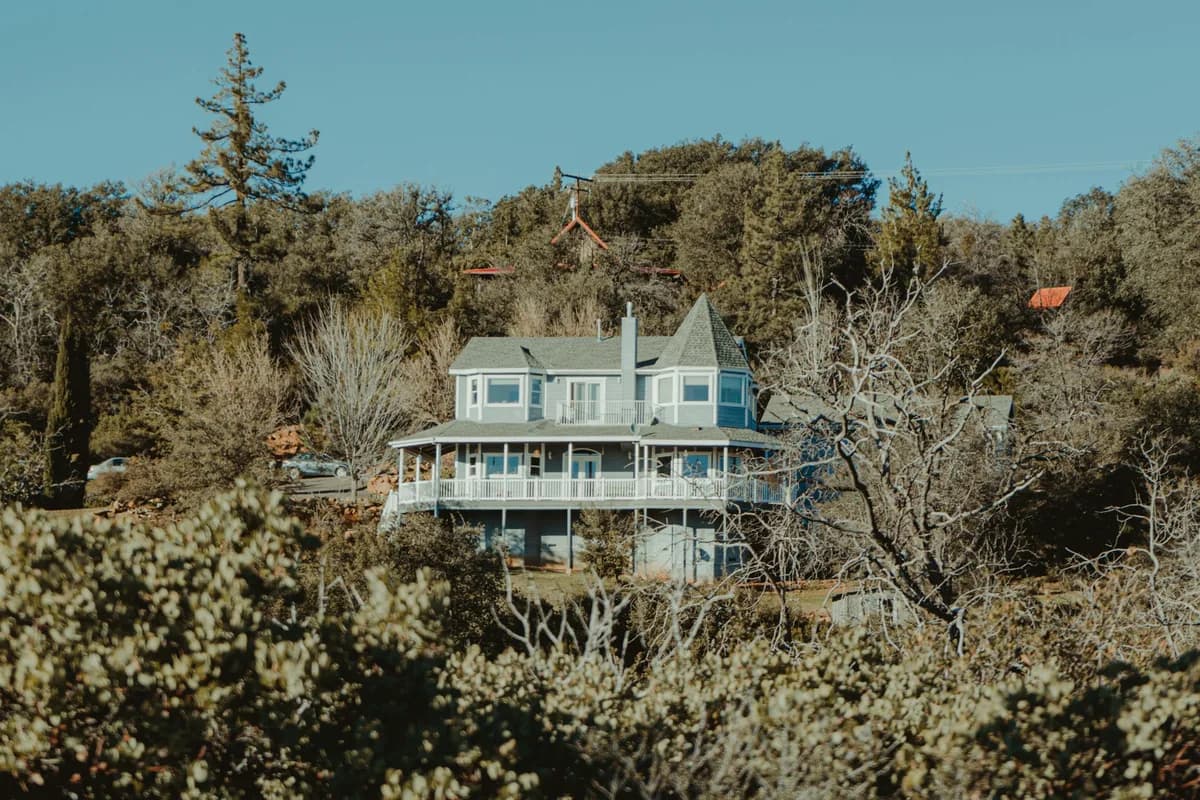 Victorian-style house surrounded by desert vegetation and trees with clear sky